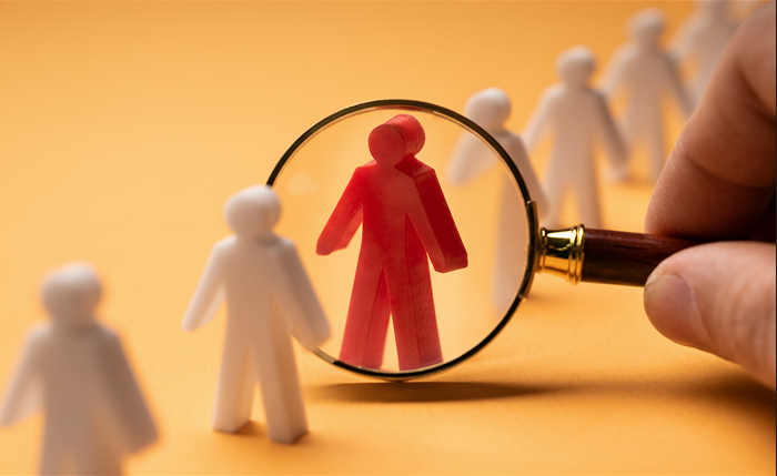 Magnifying glass focusing on a red figure representing recruitment and talent